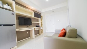 Ein modernes Wohnzimmer mit einer Couch, einem Flachbildfernseher, einer integrierten Küchenzeile mit Kühlschrank und einer Tür zu einem weiteren Raum.