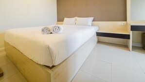 Ein modernes Hotelzimmer mit einem großen Bett, ordentlich bezogen mit weißen Leinen und gerollten Handtüchern.