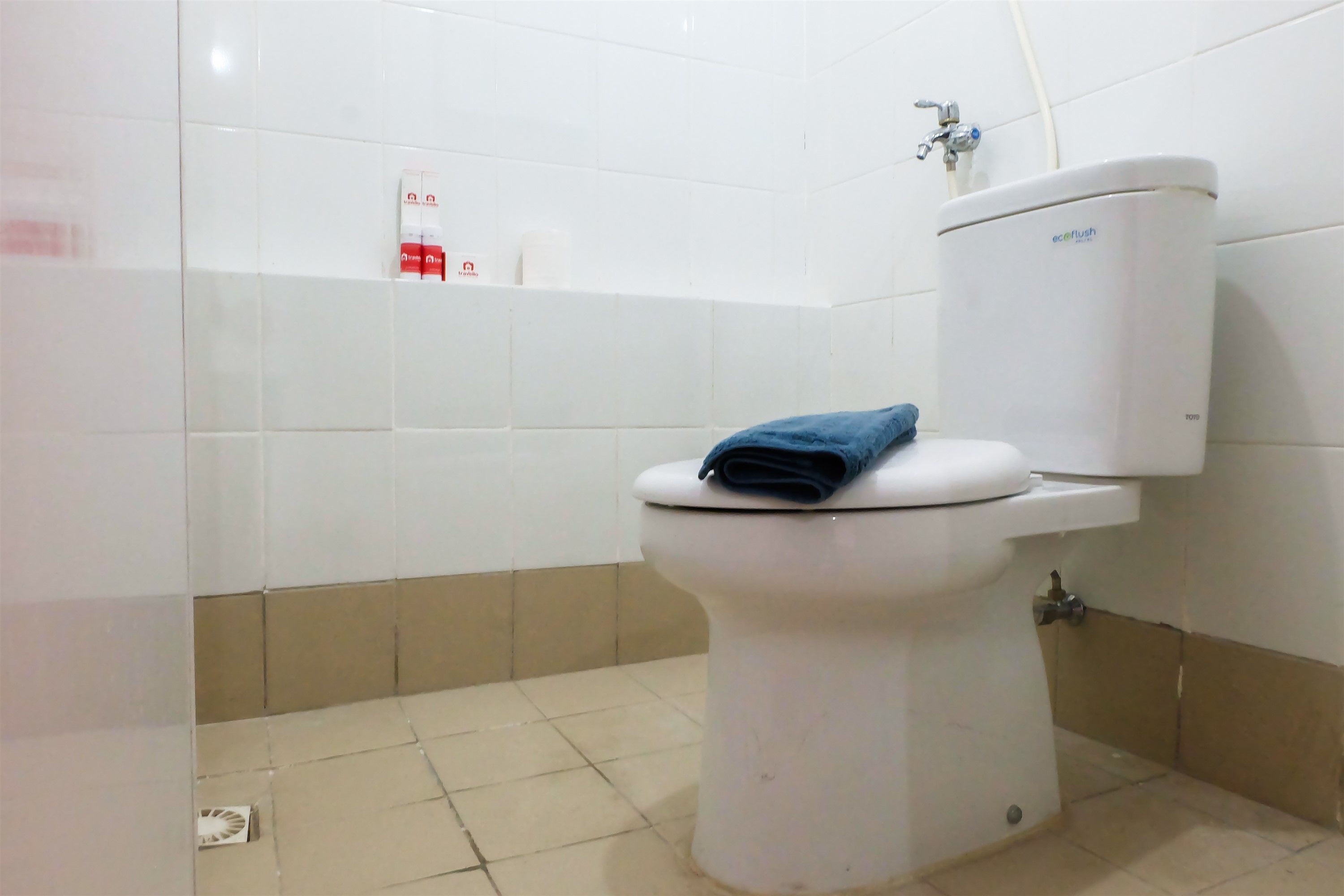 A bathroom with a white toilet, a blue towel on the seat, a white toilet paper holder, and a water heater on the floor.