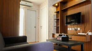 A modern living room with a sofa, a coffee table, a flat-screen TV mounted on a wooden wall, and a small table with a router and a box labeled "Lounge." - Modern Room Bassura Apartment With Direct Access To Shopping Center (Jakarta)