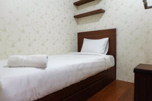 A neatly made bed with a white pillow and a rolled white towel, wooden headboard, and a small wooden nightstand. - Modern Room Bassura Apartment With Direct Access To Shopping Center (Jakarta)