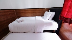 A single bed with white linens and two rolled towels, a wooden headboard, and a red curtain.