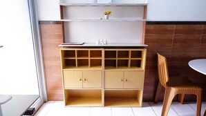 A room with a wooden cabinet with multiple compartments, a white shelf with a calendar, and a wicker chair.