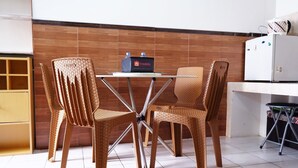 A kitchen with a white refrigerator, a small table with a laptop, wicker chairs, and a tiled floor.