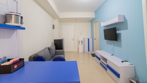 Una sala de estar moderna con un sofá, una mesa de centro, un televisor montado en la pared y una zona de cocina con estufa y dispensador de agua.