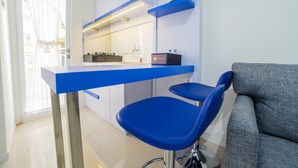 Una cocina moderna con encimeras azules, una estufa a gas y un lavamanos. Hay dos taburetes azules y un sofá gris.
