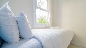 Una cama bien hecha con ropa blanca y almohadas en una habitación con ventana.