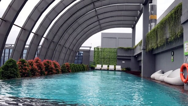 Piscina interna com design arquitetônico moderno, com vigas metálicas curvas e uma parede verde com plantas.