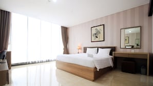 Quarto de hotel moderno com uma cama grande, mesa de cabeceira com abajur, escrivaninha, cadeira, janela ampla com cortinas e uma obra de arte emoldurada na parede.