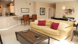 Un salon avec un canapé beige, deux fauteuils, une table basse et un coin repas comprenant une table et des chaises.