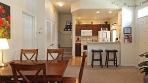 A compact kitchen with white cabinets, a microwave, and a refrigerator. There is a dining area with a wooden table and chairs. - Lc2604 - Villas at Seven Dwarfs Lane - 4 Bed 3 Baths Townhome (Kissimmee)