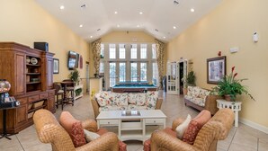 A spacious living room with a pool table, comfortable seating, and a large window providing natural light. - Lc2604 - Villas at Seven Dwarfs Lane - 4 Bed 3 Baths Townhome (Kissimmee)