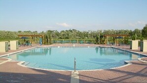 A rectangular pool with a tiled deck surrounding it, two pergolas with umbrellas, and a backdrop of trees. - Lc2604 - Villas at Seven Dwarfs Lane - 4 Bed 3 Baths Townhome (Kissimmee)