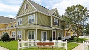 A two-story house with a front porch, a picket fence, and a bench. - Lc2604 - Villas at Seven Dwarfs Lane - 4 Bed 3 Baths Townhome (Kissimmee)