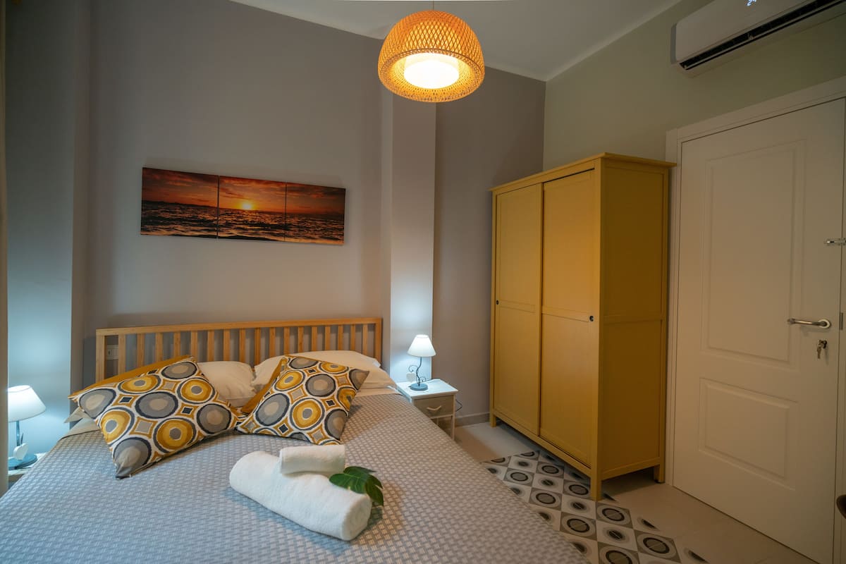 Een slaapkamer met een bed, nachtkastje met lamp, kast en een schilderij aan de muur.