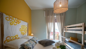 Una camera da letto con un letto a castello, un letto grande con molti cuscini, una lampada a sospensione e una finestra con tende.
