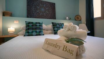 A neatly made bed with a towel and a 'Laundry Bag' sign, pillows, a wall art piece, and a bedside lamp.