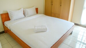A neatly made bed with white linens and a rolled towel, wooden headboard, and a wardrobe with two doors. - Apartment Taman Semanan Cengkareng Great Value (Jakarta)