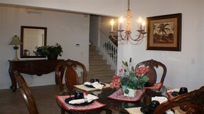 A dining area with a glass table, chairs, a chandelier, a staircase, and a framed picture on the wall.