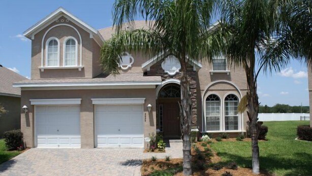 A two-story house with a brick facade, two garage doors, and a landscaped front yard with a palm tree. - Ip60402 - Sand Hill - 5 Bed 3 Baths Villa (Davenport)