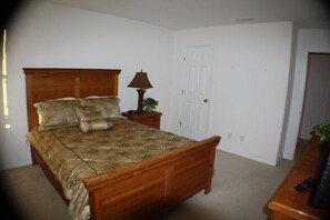 A bedroom with a wooden bed, a bedside table with a lamp, and a door.