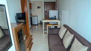 A living room with a brown sofa, a TV, a small table, and a refrigerator. - Best Price Grand Palace Near JIEXPO Kemayoran (Jakarta)