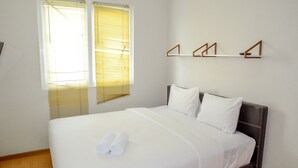 A neatly made bed with white linens and rolled towels, a wooden headboard, and a wall-mounted shelf with three wooden brackets. - Best Price Grand Palace Near JIEXPO Kemayoran (Jakarta)