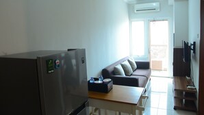 A compact living space with a kitchenette, a sofa, a wooden table, and a TV mounted on the wall. - Best Price Grand Palace Near JIEXPO Kemayoran (Jakarta)