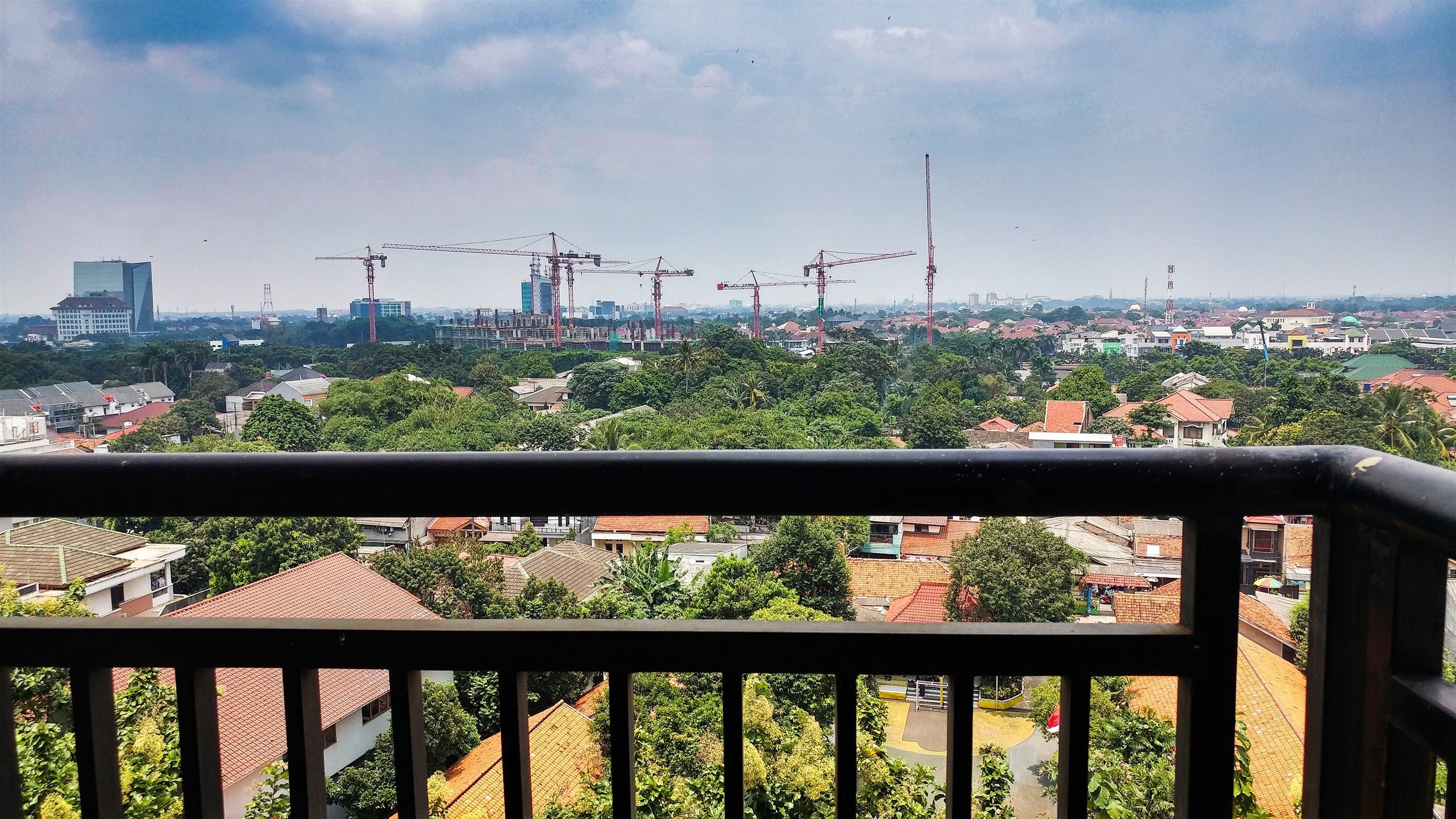 Un balcón con vistas a un paisaje urbano, que incluye edificios residenciales y grúas de construcción.