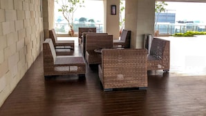 A covered outdoor seating area with wicker furniture and a wooden floor. - Exclusive Studio at Menteng Park Apartment (Jakarta)