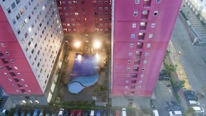 Un immeuble de grande hauteur, doté de nombreux étages, une cour intérieure avec une piscine bleue et un espace de stationnement où sont garées plusieurs voitures.