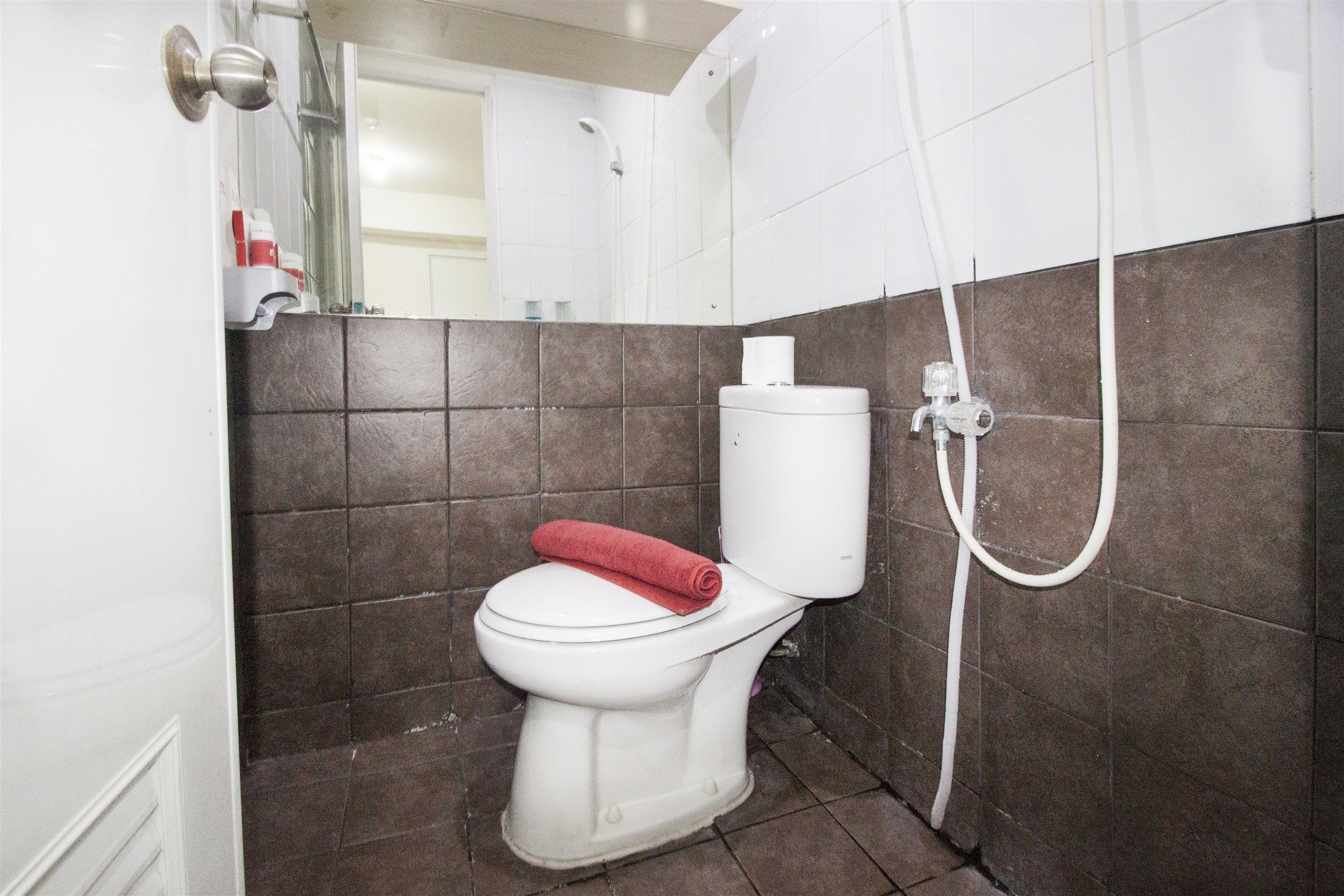 A bathroom with a white toilet, a shower, and brown tiled walls.
