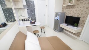 Un espace de vie compact comprenant un canapé, un petit coin cuisine, une télévision et un réfrigérateur.