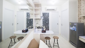 Une cuisine moderne dotée d’un îlot central, de meubles blancs et d’un réfrigérateur. L’îlot est agrémenté de deux tabourets et d’un banc.