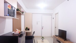 Un espacio habitable pequeño con kitchenette, un sofá, un televisor sobre un soporte de madera y una puerta con cerradura.