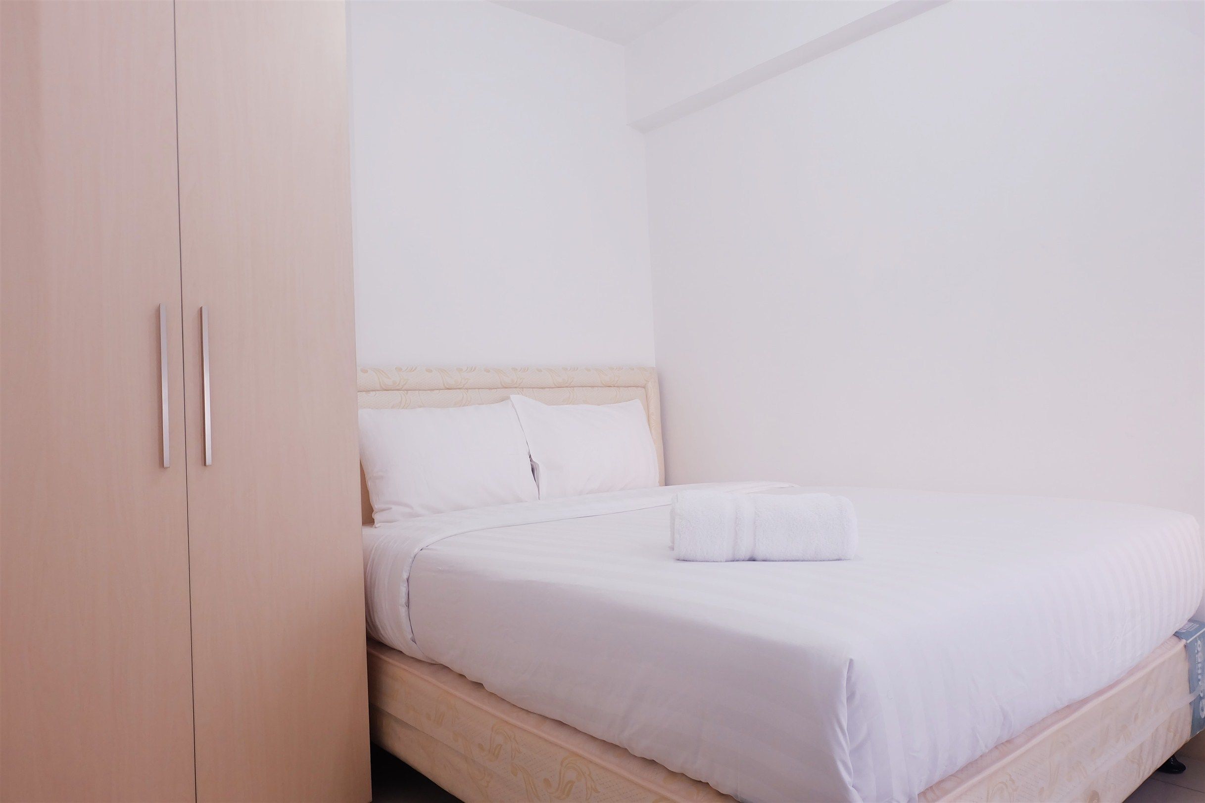Un lit simple avec du linge de lit blanc et une tête de lit en bois, dans une pièce où se trouve une armoire de couleur claire.