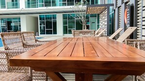 A wooden table and wicker chairs in an outdoor setting with a modern building in the background. - Best Price Brooklyn Apartment near IKEA Alam Sutera (South Tangerang)