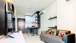 A modern living room with a grey sofa, a flat-screen TV, and a kitchen area with a bar stool. - Best Price Brooklyn Apartment near IKEA Alam Sutera (South Tangerang)