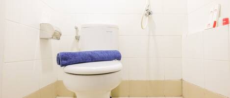 A white toilet with a blue towel on top, a hand dryer, and a shower hose in a bathroom with white tiles.