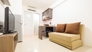 A compact living space with a sofa, a television, a kitchenette, and a door leading to another room. - Enjoy Jakarta! Bassura City Apartment (Jakarta)