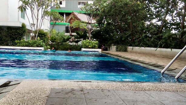 A swimming pool with clear blue water, surrounded by pebbles and a metal ladder. - Enjoy Jakarta! Bassura City Apartment (Jakarta)
