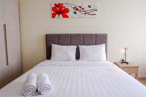 A neatly made bed with white linens and rolled towels, a grey upholstered headboard, and a bedside table with a lamp. - New Furnished Studio Menteng Park Apartment (Jakarta)