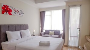 Hotellihuone, jossa on suuri sänky, sohva, seinällä taulu ja ovi, joka johtaa parvekkeelle.