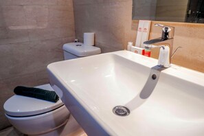 A bathroom with a white sink, toilet, and a towel on the toilet seat. - New Furnished Studio Menteng Park Apartment (Jakarta)