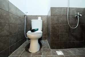 A bathroom with a toilet, a shower, and a wall-mounted toilet paper holder. - Easy Access to Mall Green Pramuka Apartment (Jakarta)