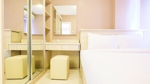 A hotel room with a bed, a mirror, a vanity with a mirror, and two ottomans. - Easy Access to Mall Green Pramuka Apartment (Jakarta)