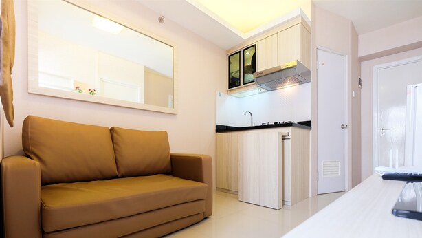 A modern living room with a sofa, a kitchen area with cabinets and a countertop, and a door leading to another room. - Easy Access to Mall Green Pramuka Apartment (Jakarta)