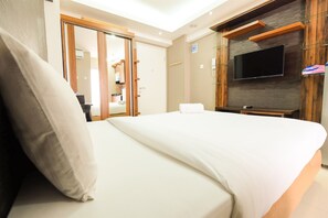 A hotel room with a large bed, a TV mounted on the wall, and a wooden wardrobe. - Simple Studio Bassura City Apartment (Jakarta)