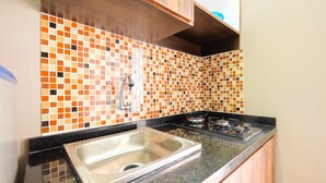 Een keuken met een betegelde spatwand, een RVS spoelbak en een gasfornuis.