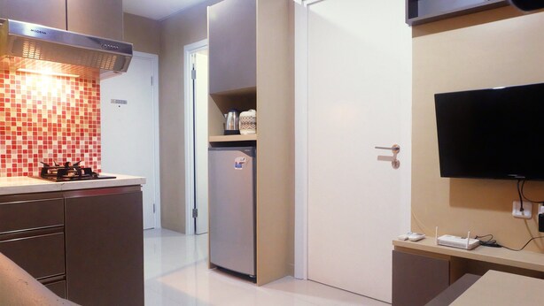 A compact kitchen with a built-in stove, a refrigerator, and a flat-screen TV mounted on the wall.